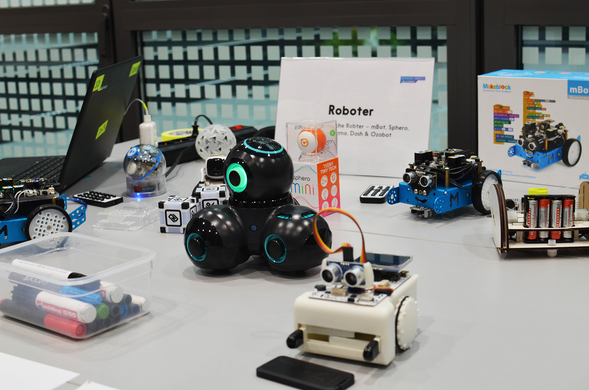 Auf einem Tisch sind Roboter angeordnet, die über verschiedene Funktionen verfügen. Diese Roboter dienen als Werkzeug zur Vermittlung von Programmierungskompetenzen und Technikverständnis.
