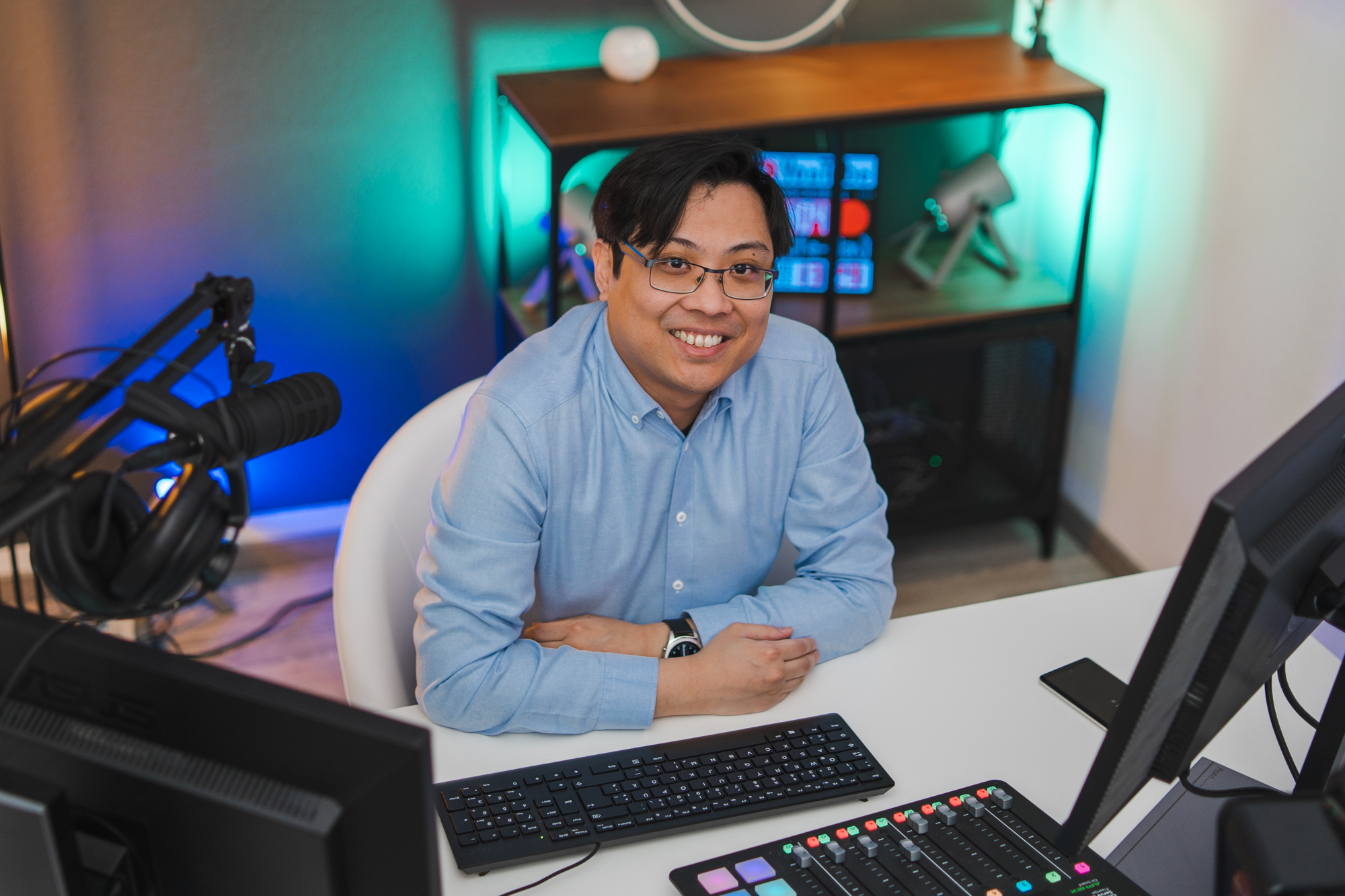 Porträt von Kok Hung Cheong. Er sitzt an einem Schreibtisch und schaut lächelnd in die Kamera.