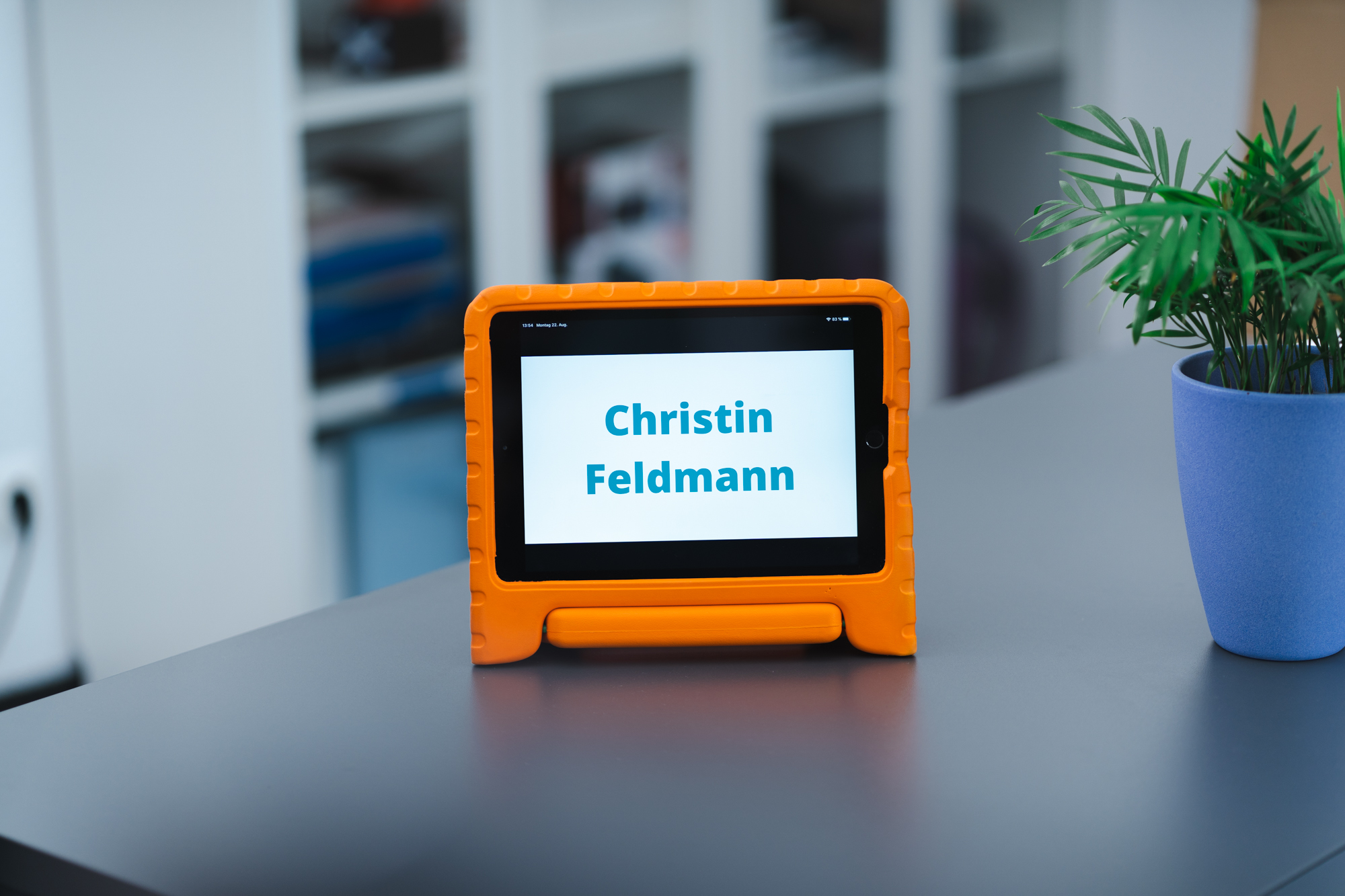 Zu sehen ist ein iPad auf einem Schreibtisch. Das iPad zeigt den Namen Christin Feldmann.