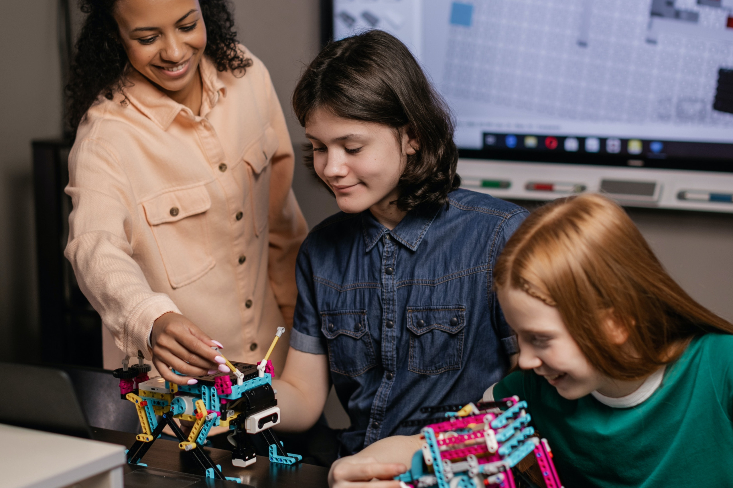 Zwei Jugendliche bauen Roboter und werden dabei von einer Pädagogin unterstützt.