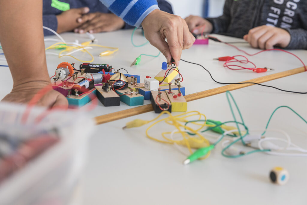 Hände arbeiten mit Kabeln und Programmierblöcken.